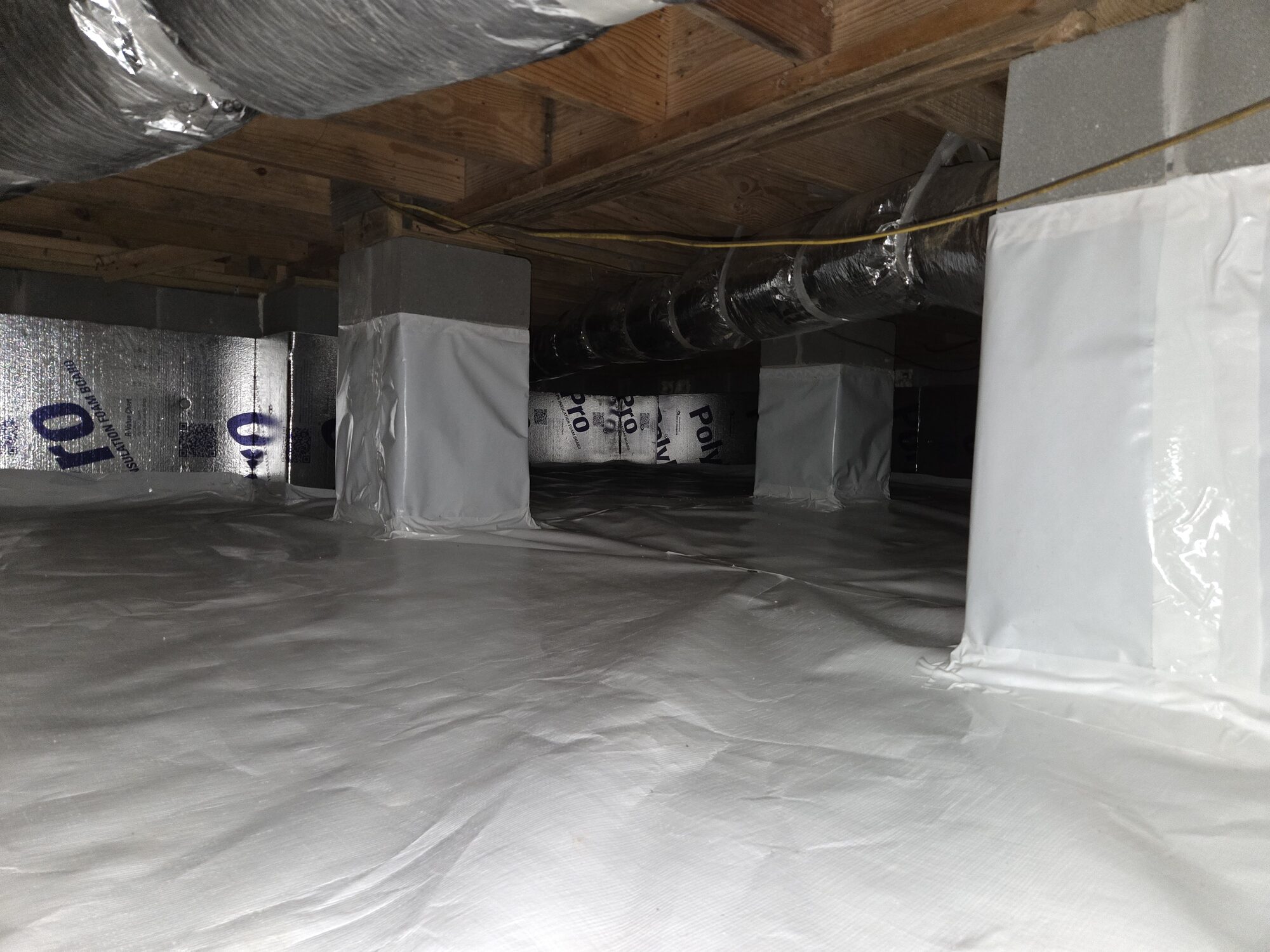 Same crawlspace after full encapsulation with a clean white vapor barrier, wrapped support piers and sealed foam board walls