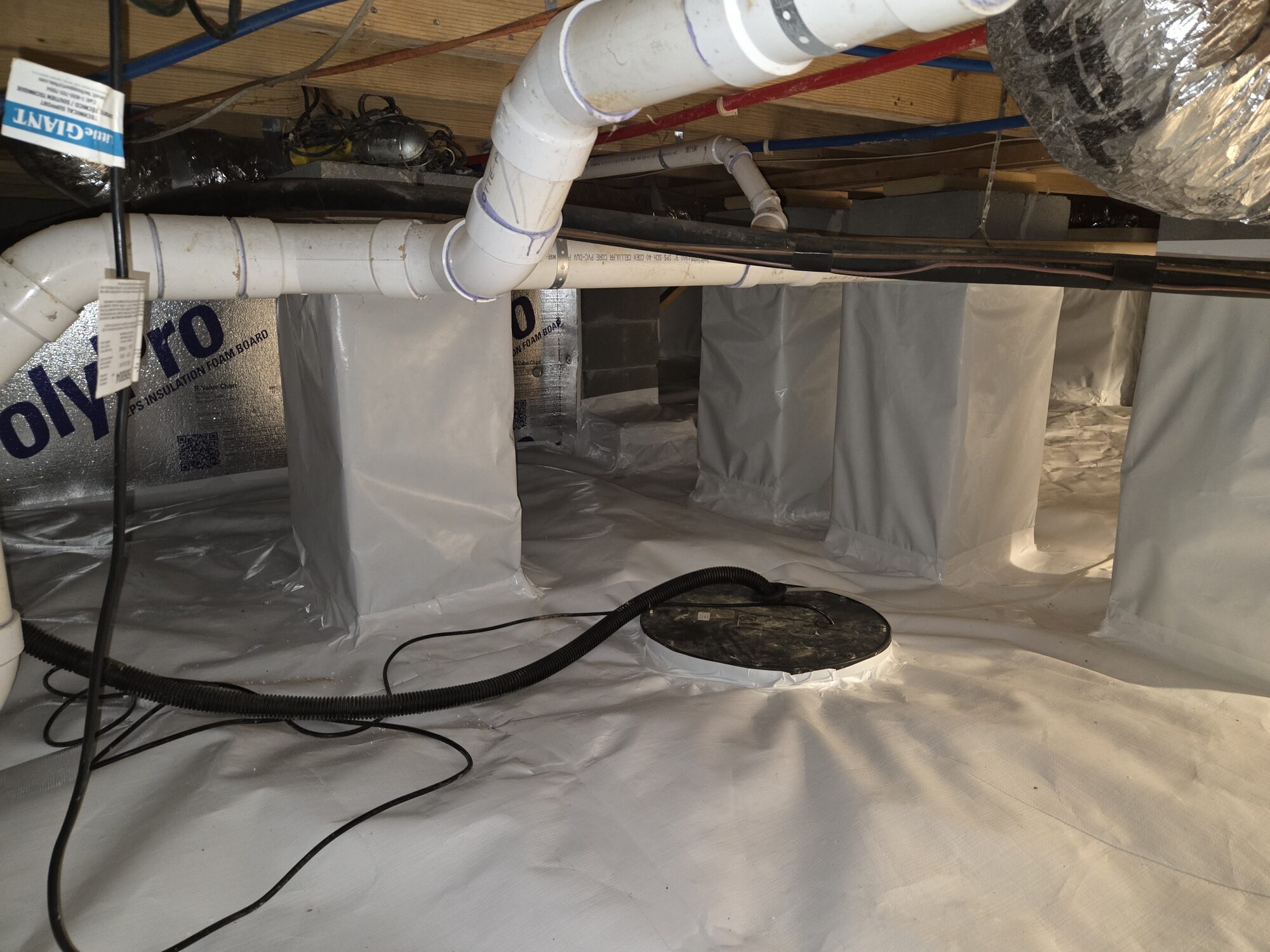 Crawlspace after service with a clean white vapor barrier covering the floor, wrapped piers and a sealed sump pump lid