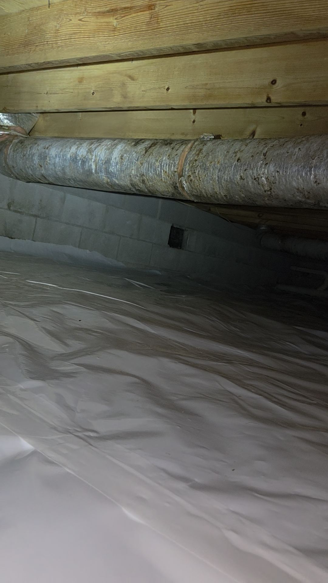 Same crawlspace after service with the failing insulation cleared out and a clean liner sealed along the foundation wall