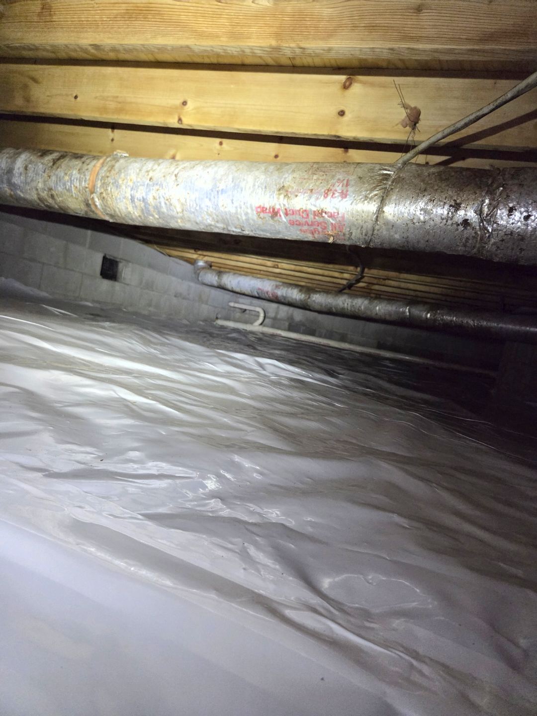 Same crawlspace after service with a clean sealed liner and freshly wrapped ductwork along the joists