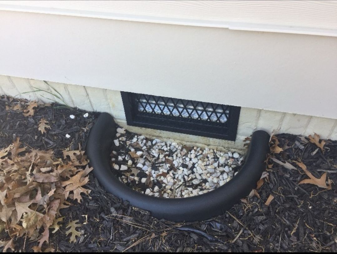 Same foundation vent after drainage work with a gravel bed and fresh mulch finished around the extension pipe