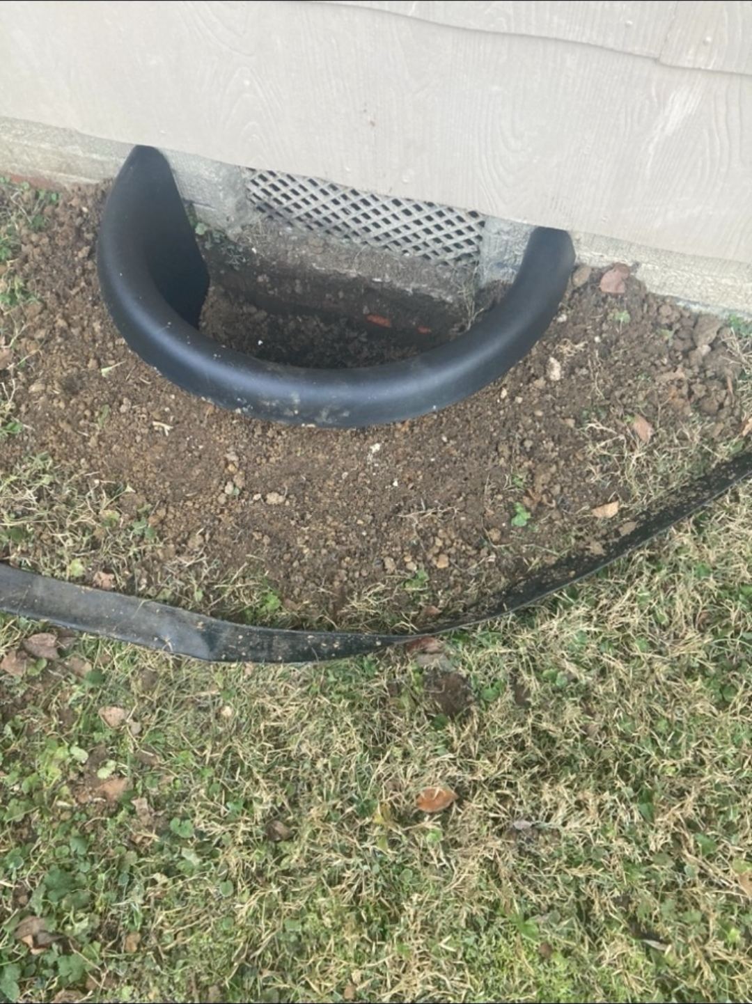 Foundation vent before drainage work with bare dirt around an exposed extension pipe running from the crawlspace vent