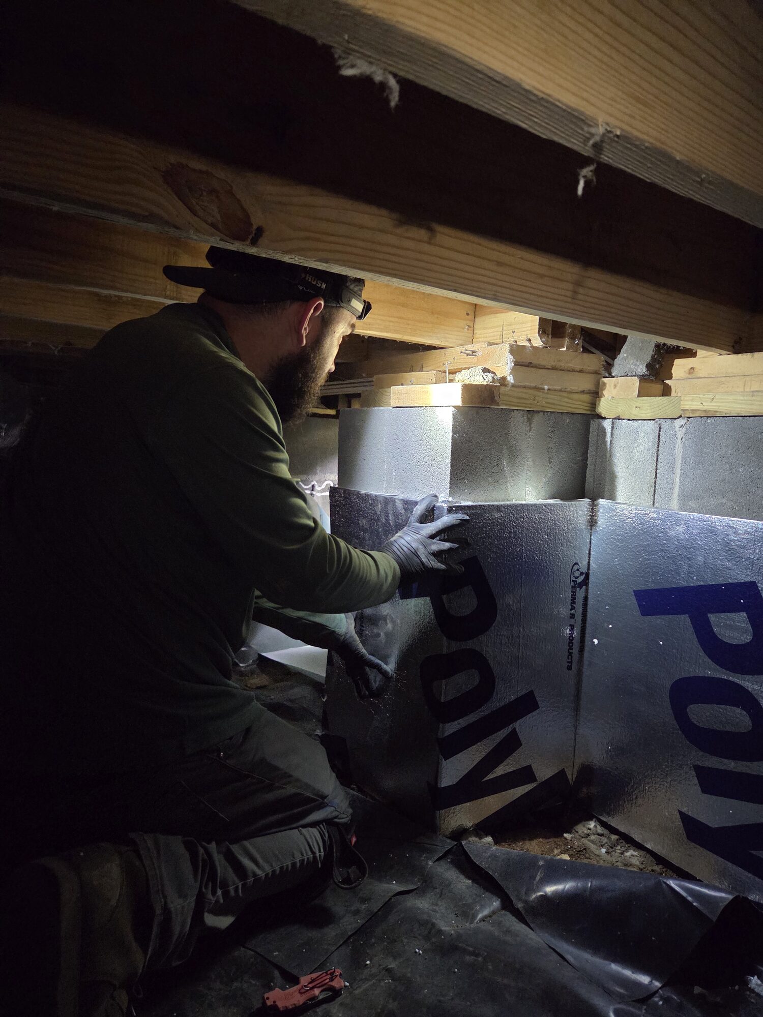 Crawlspace Cowboys technician installing rigid foam insulation board against the foundation walls during an encapsulation job