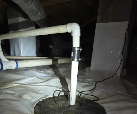 Sump pump basin with sealed lid and PVC discharge line installed through the white vapor barrier in a crawlspace